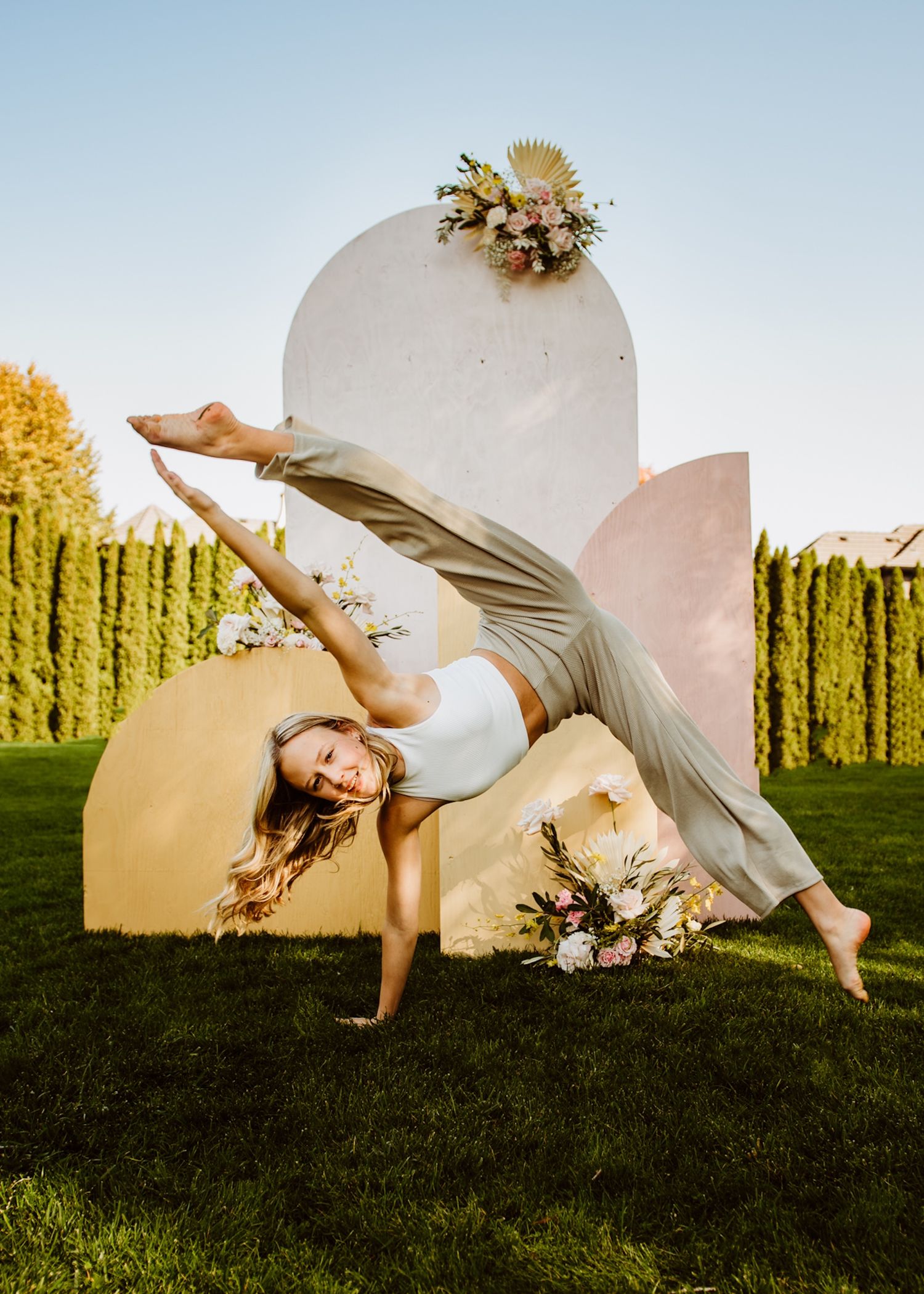 Dancer gracefully posing against a curved white backdrop with floral decorations in an outdoor garden setting.