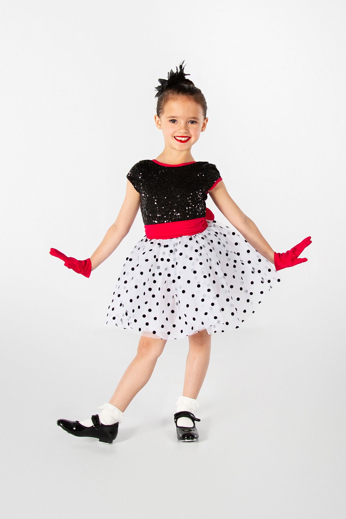 A dancer in a festive polka dot dress with red gloves and black tap shoes poses against a white backdrop.