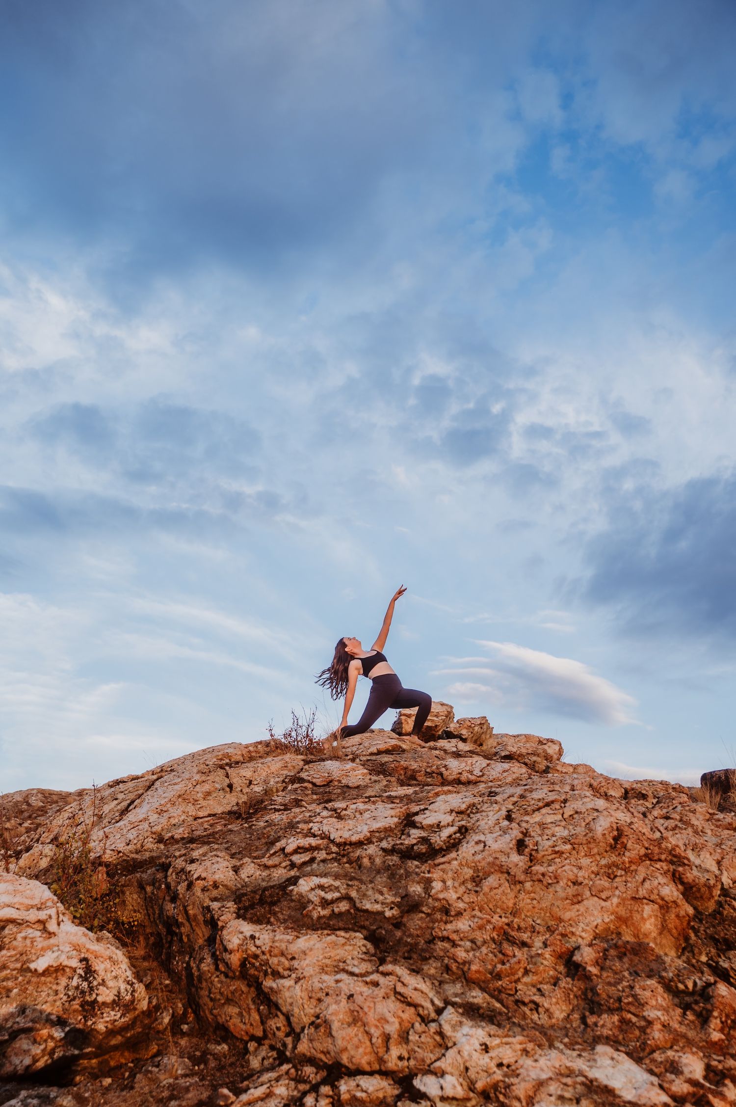 Athletic dance pose performed on rocky terrain against dramatic cloudy sky at sunset.