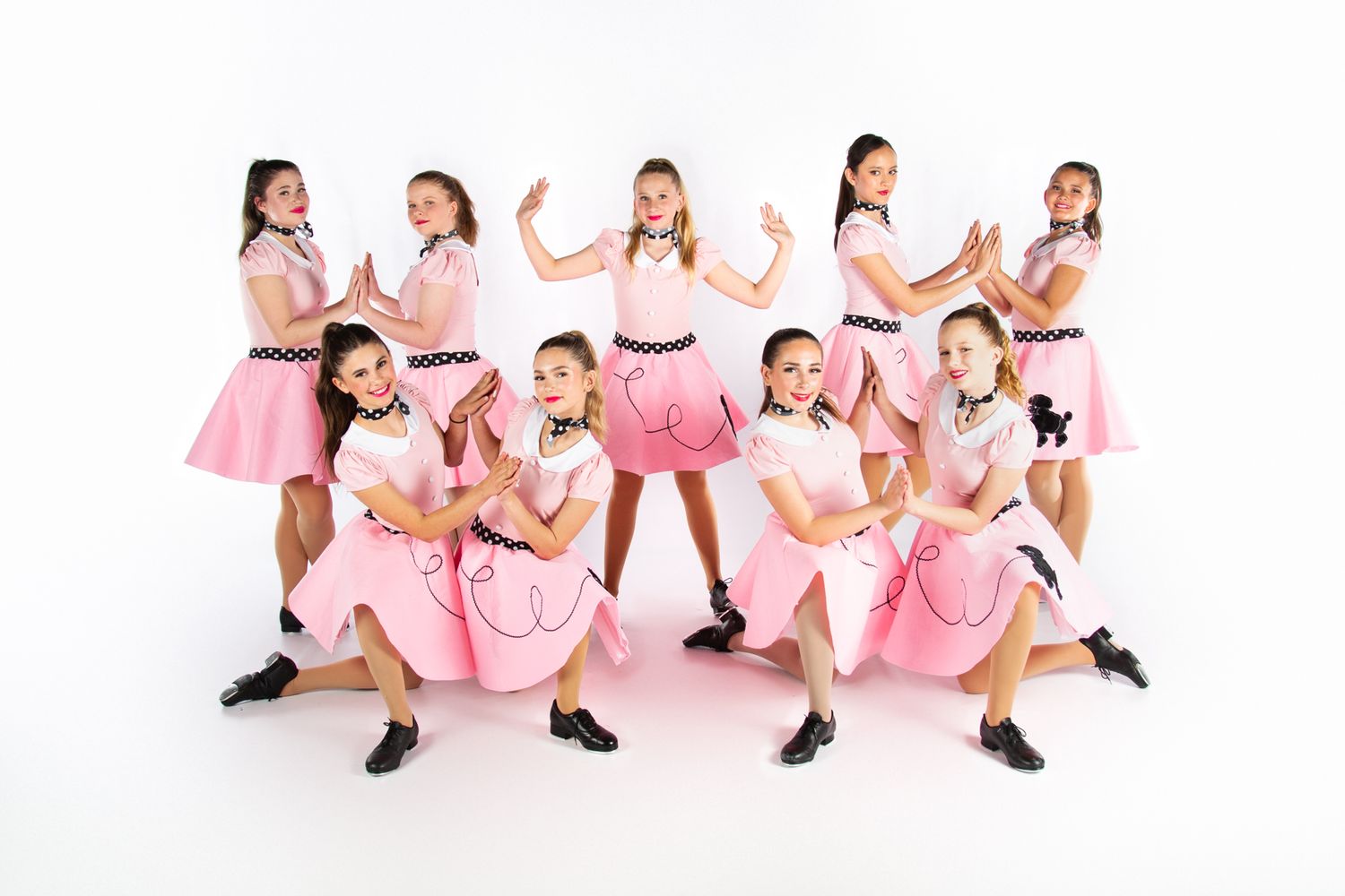 Dance troupe in matching pink dresses performs choreographed routine on white background.