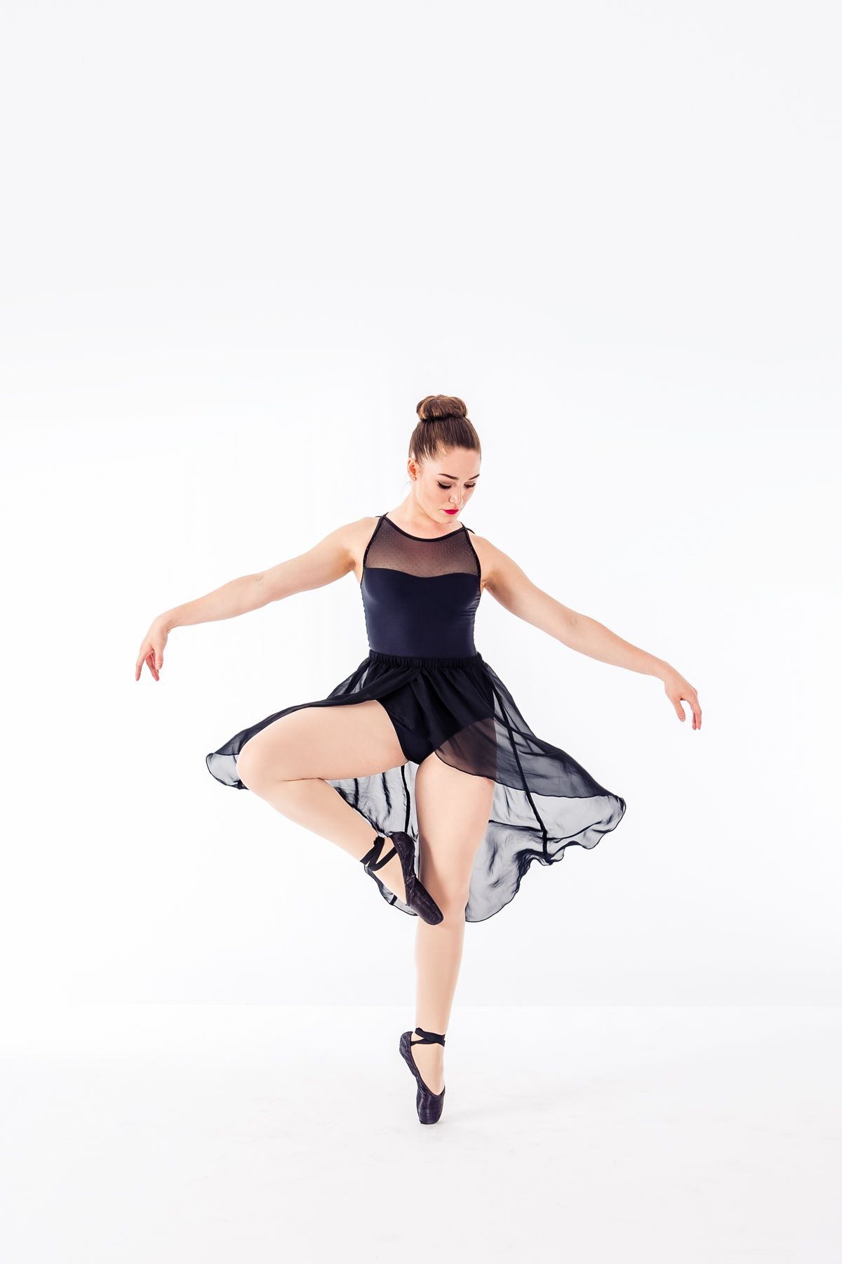 Dancer in black tulle dress performs elegant turn on pointe shoes in studio setting.