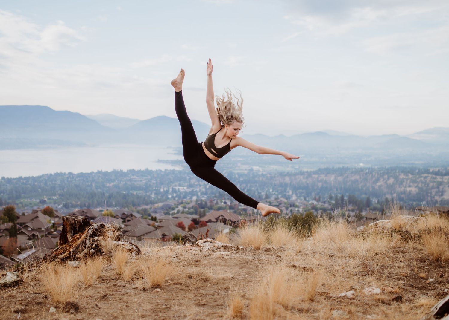 A dancer leaps gracefully through the air against a scenic mountain landscape background in dry grassland terrain.