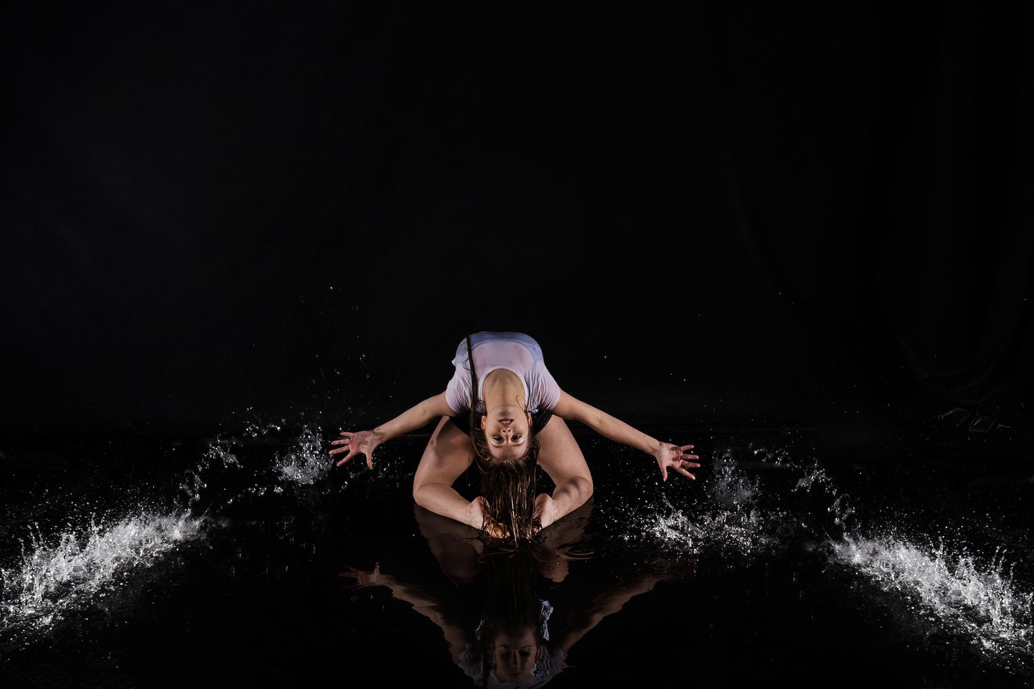 Dancer in purple outfit creates dramatic water splash effect against black background during dynamic performance.