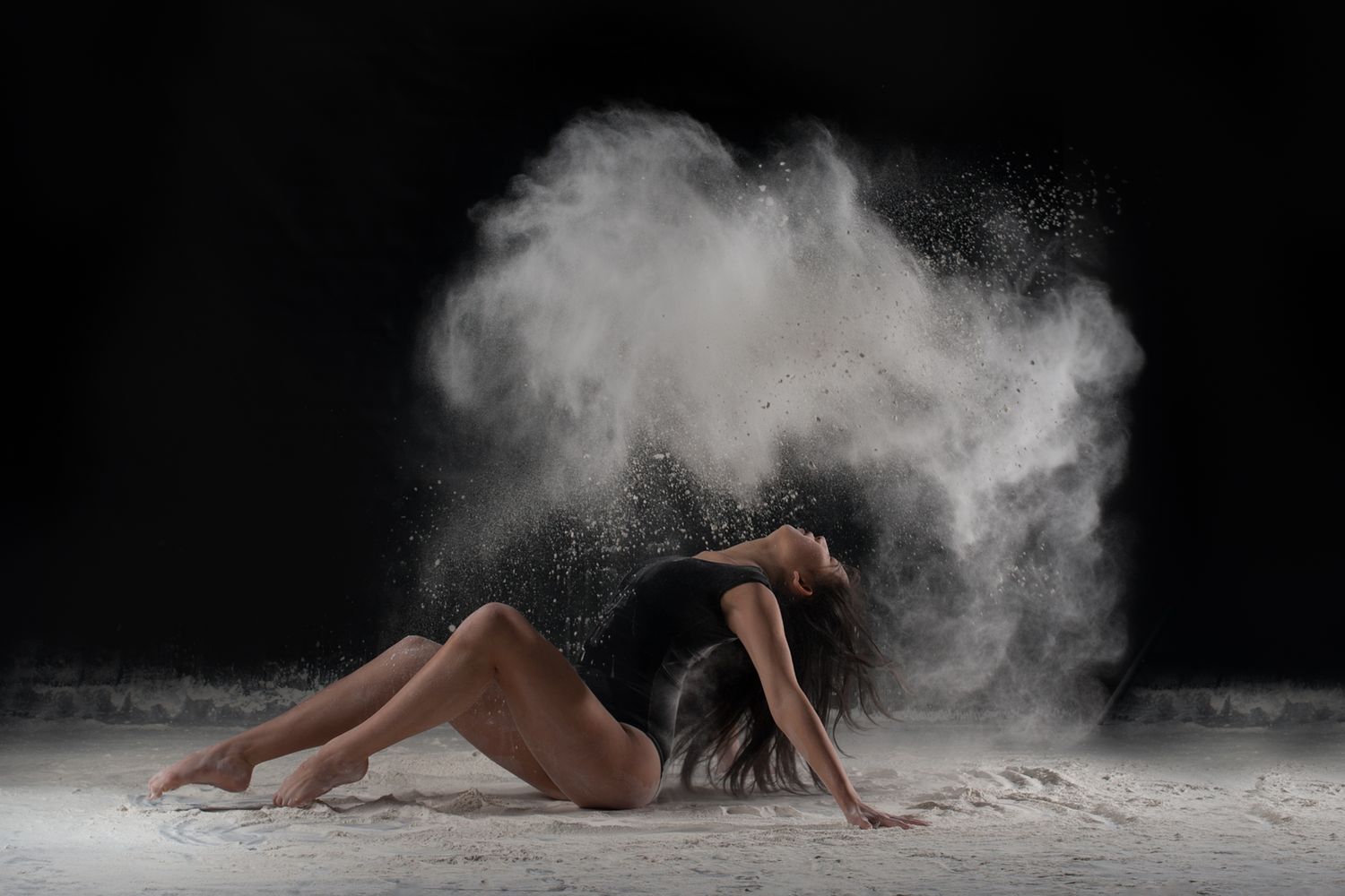 Dancer creates dramatic cloud effect while moving through white powder on dark background.