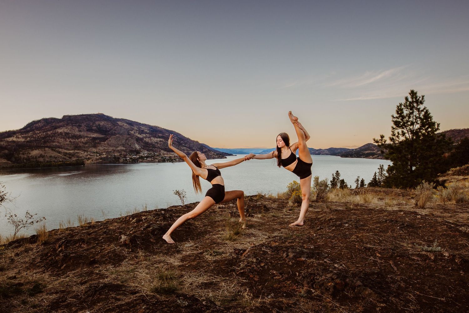 Two dancers perform graceful poses against a scenic mountain lake backdrop at sunset.