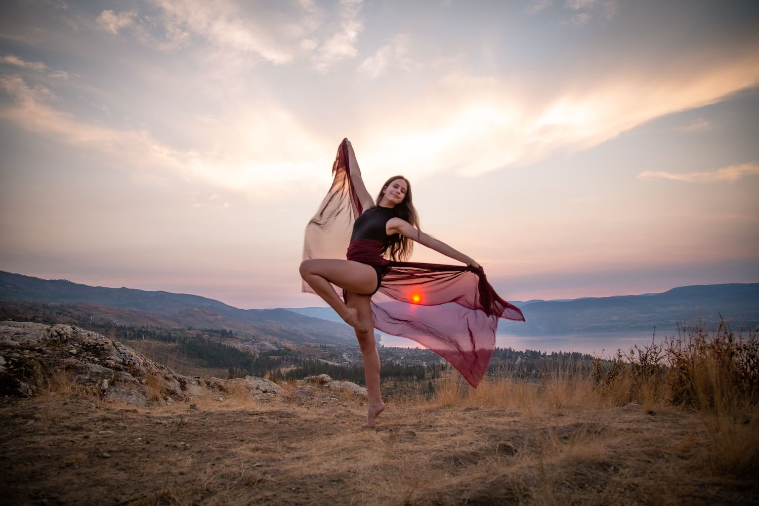 Elegant dance pose with flowing fabric performed at sunset on mountain terrain.