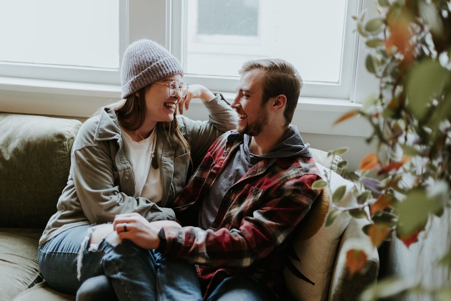 Couple sharing intimate moments and laughter while sitting together on a couch near a window.