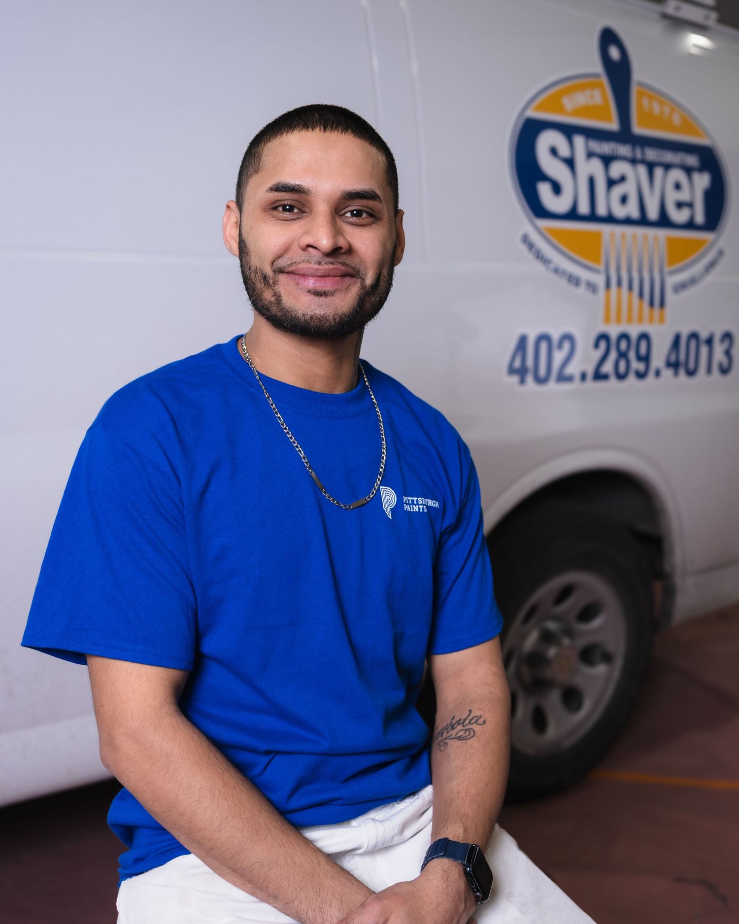 A smiling man in a blue shirt sits in front of a Shaver Painting & Decorating company van in Omaha, NE.