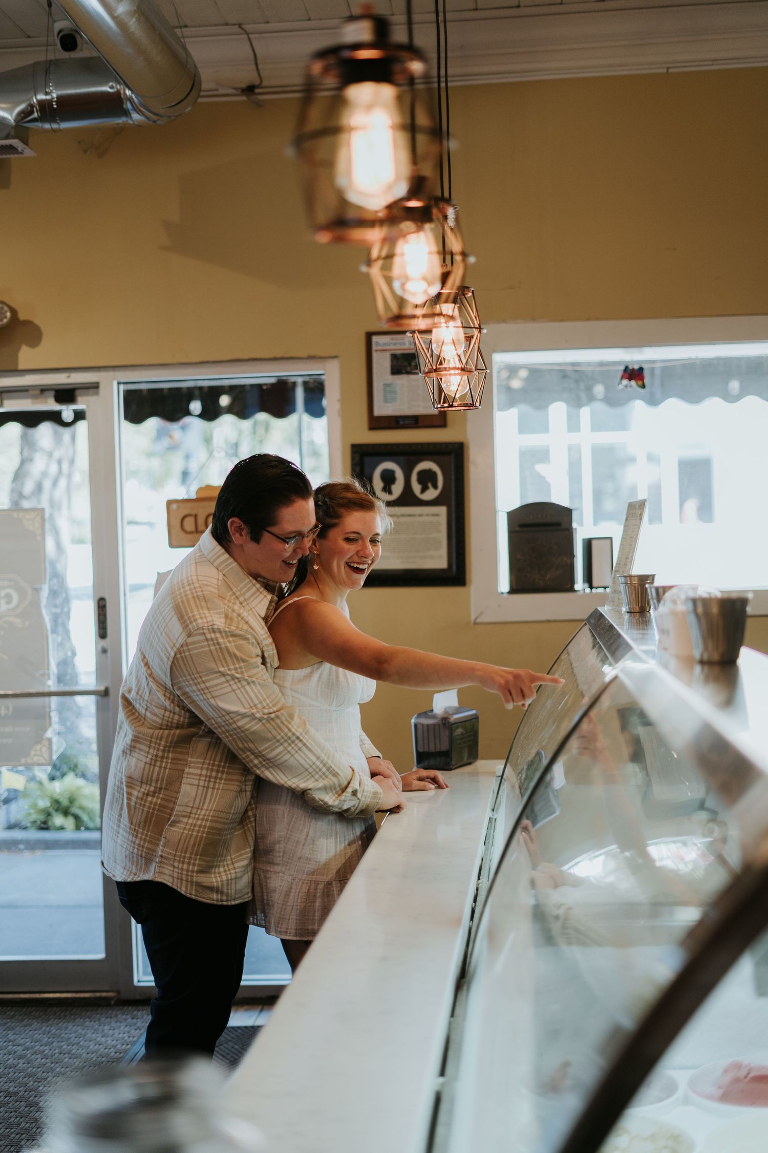 A couple looks at items in a display case under vintage lantern lighting in a rustic cafe setting.
