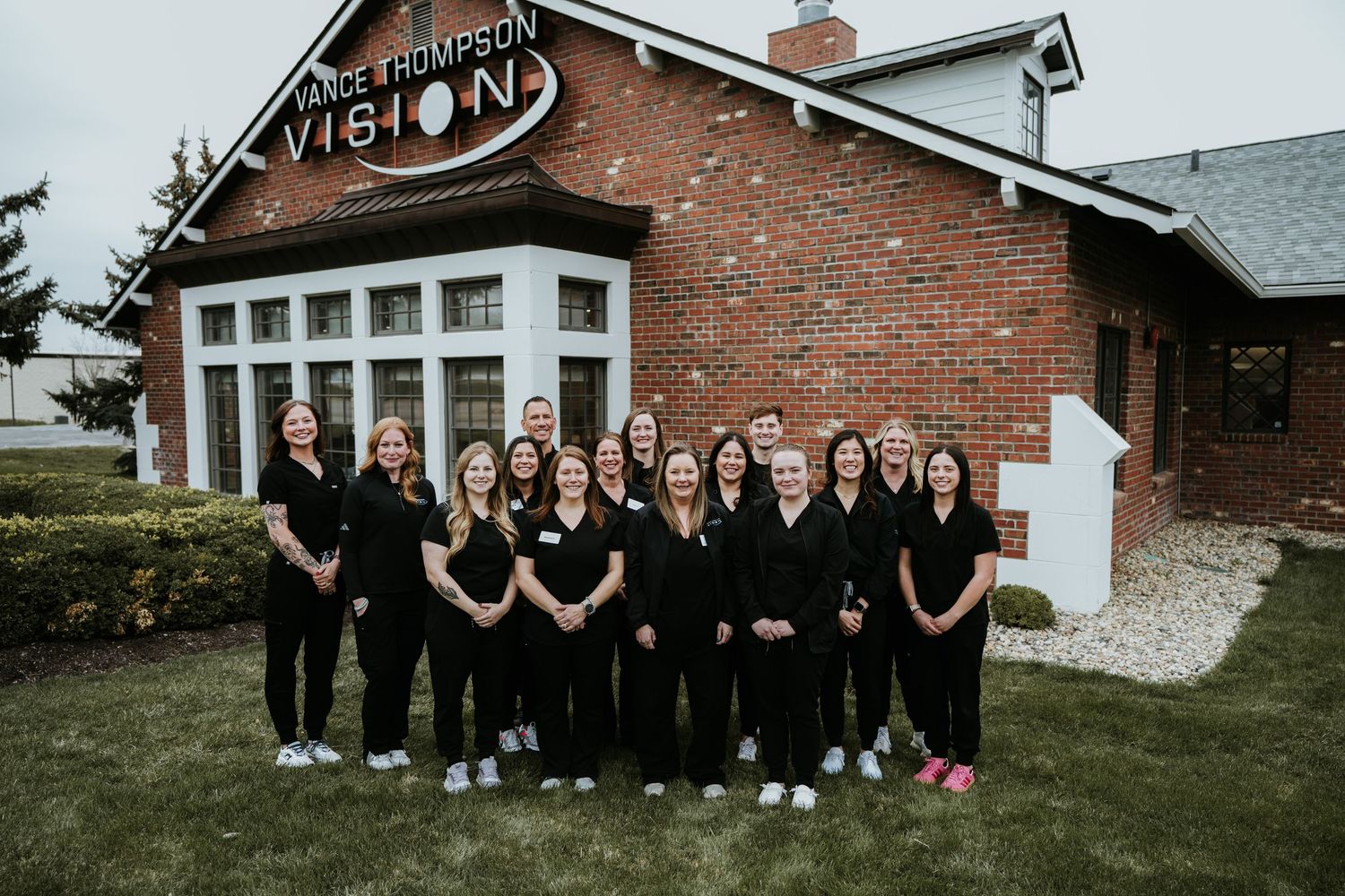 Thompson Vision eye care team in black uniforms posing outside their brick office building.