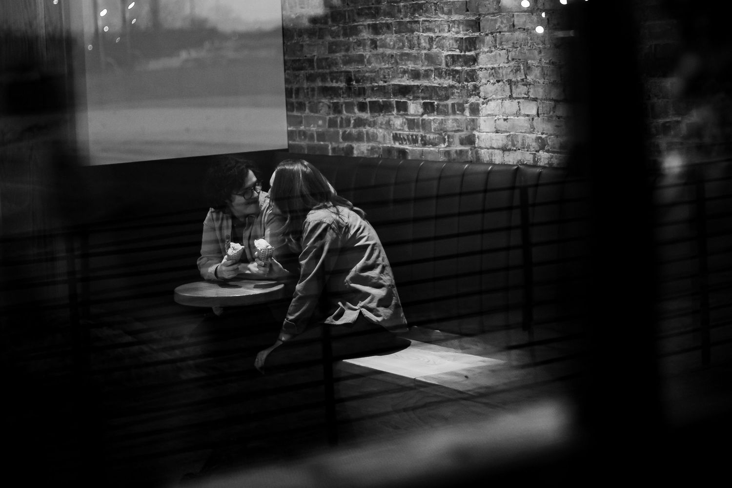 Black and white photograph showing people studying at tables in a dimly lit room with brick walls.