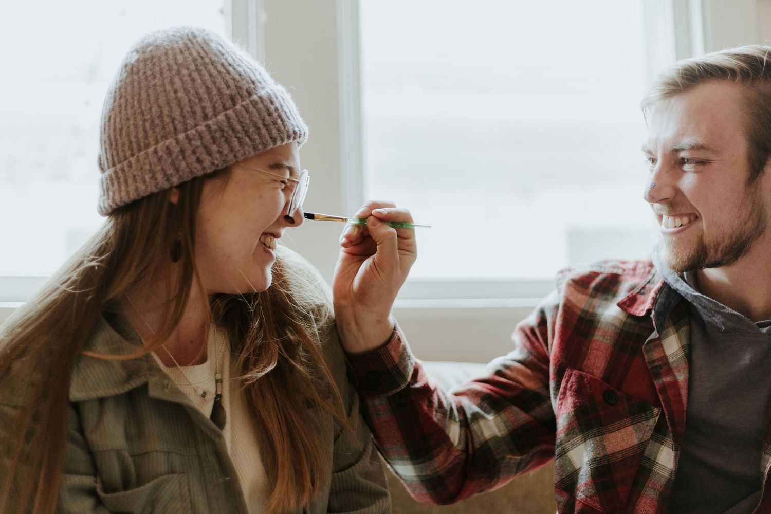 Two people lean close together while sharing drinks by a window in warm natural light.