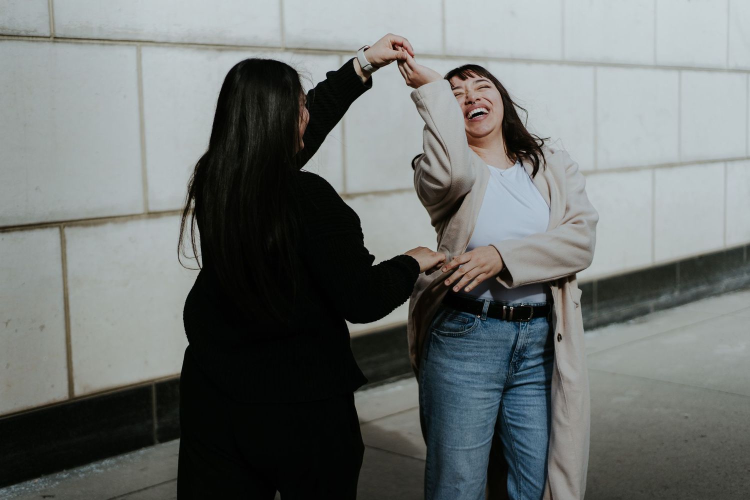 Two people sharing laughter and joy while standing against a white wall background.