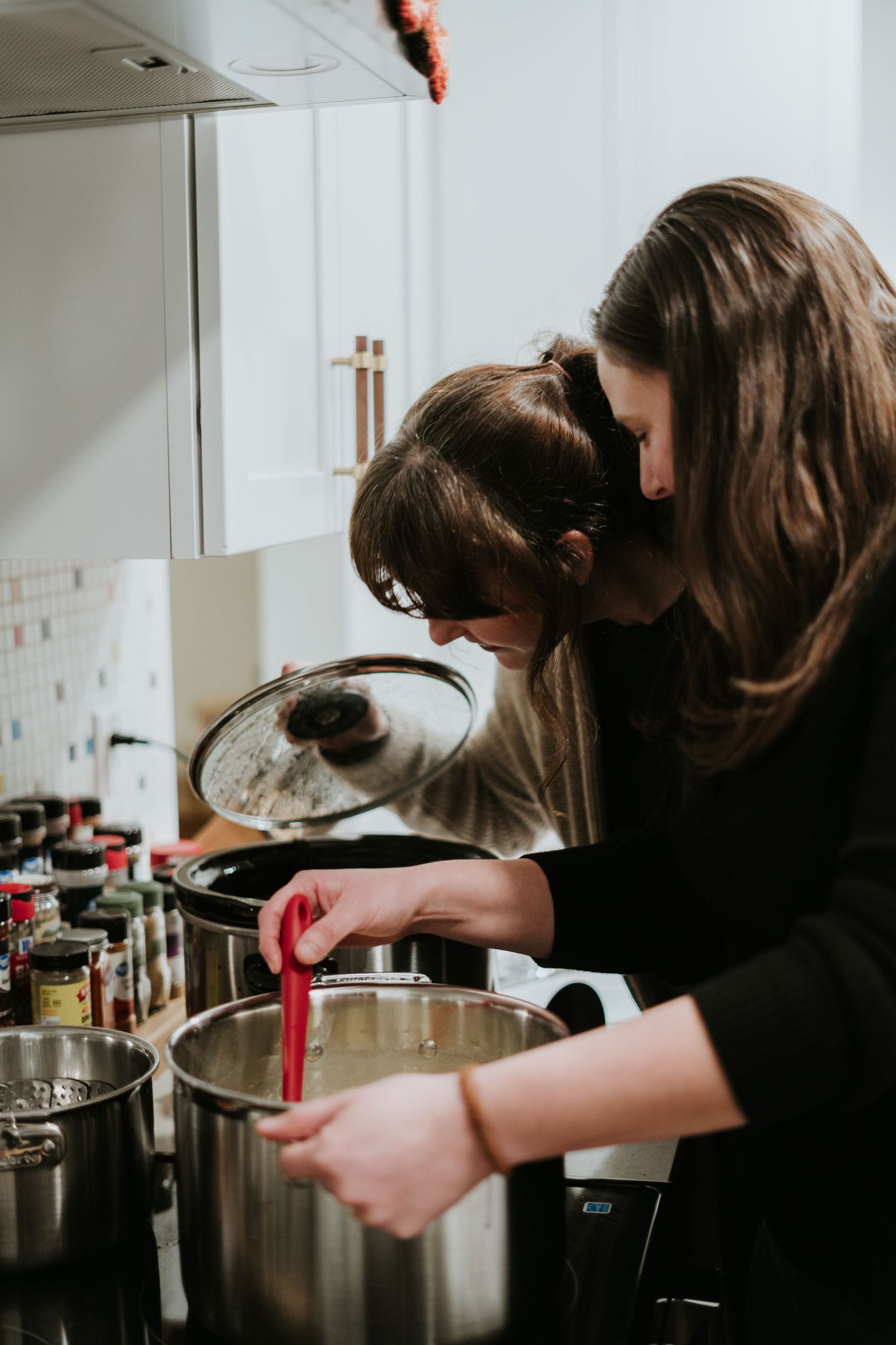 A person in dark clothing carefully stirs a pot on a stovetop while cooking in a bright kitchen.