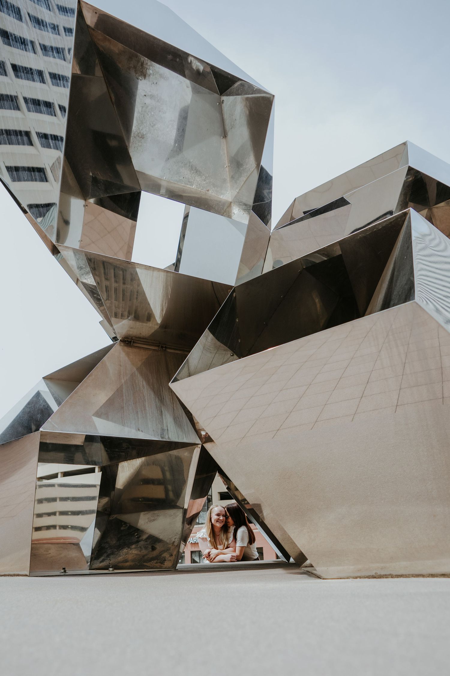 Modern geometric architectural sculpture with angular mirrored surfaces creates dramatic reflections against a white backdrop.