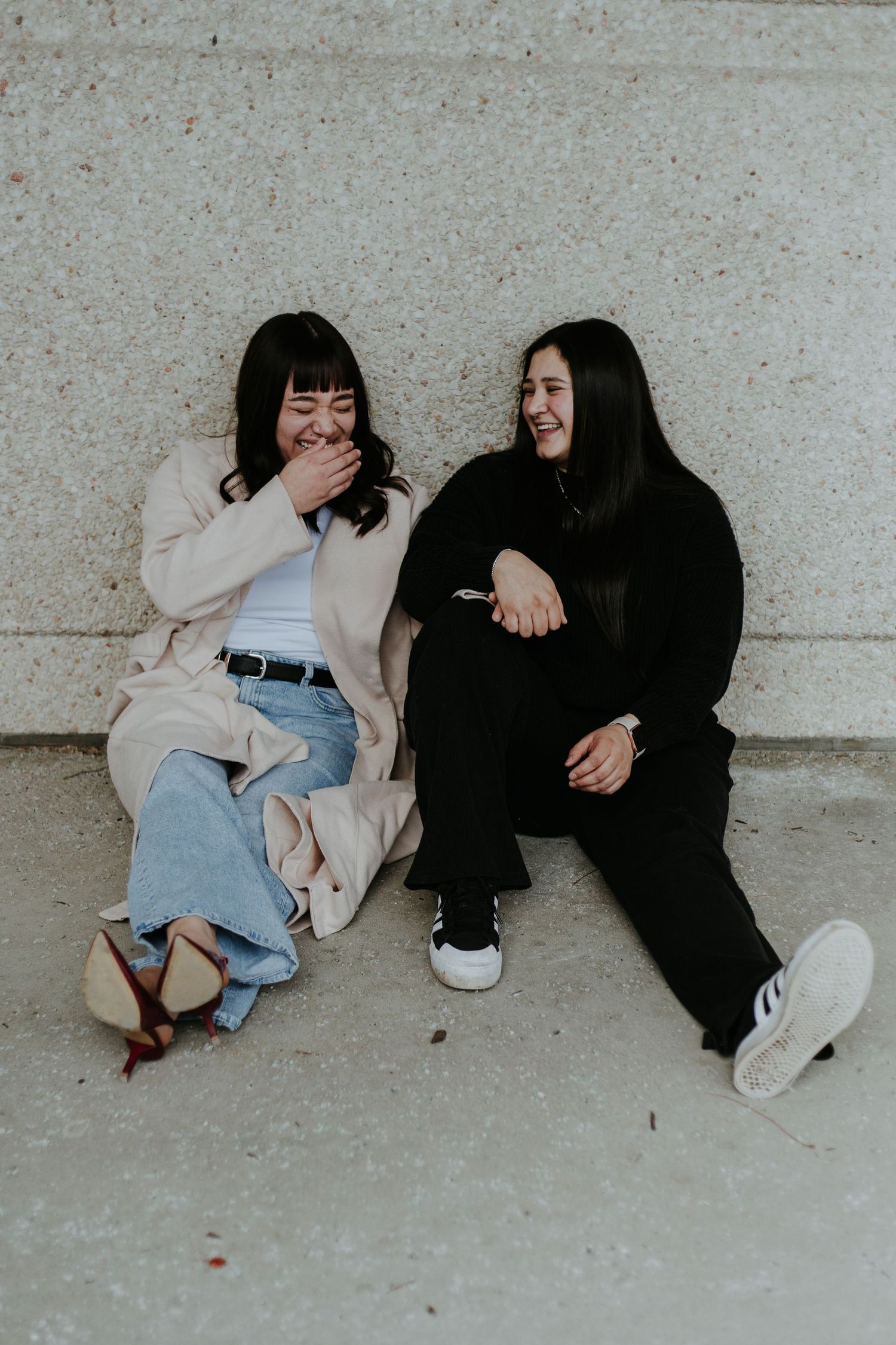Three people in casual attire sit and relax against a concrete wall in an artistic composition.