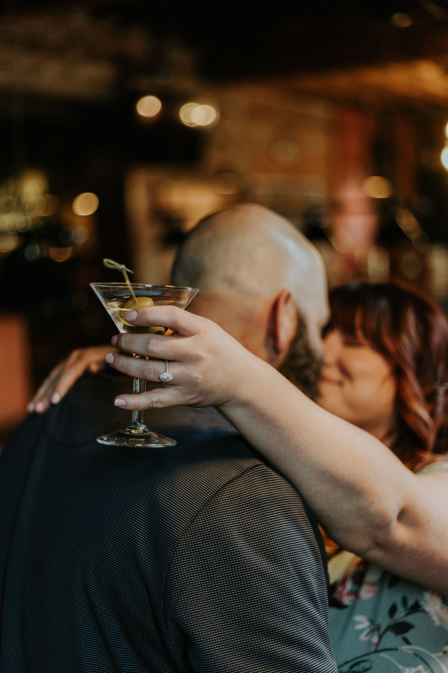 Hand holding a martini glass with cocktail against a blurred bar background.