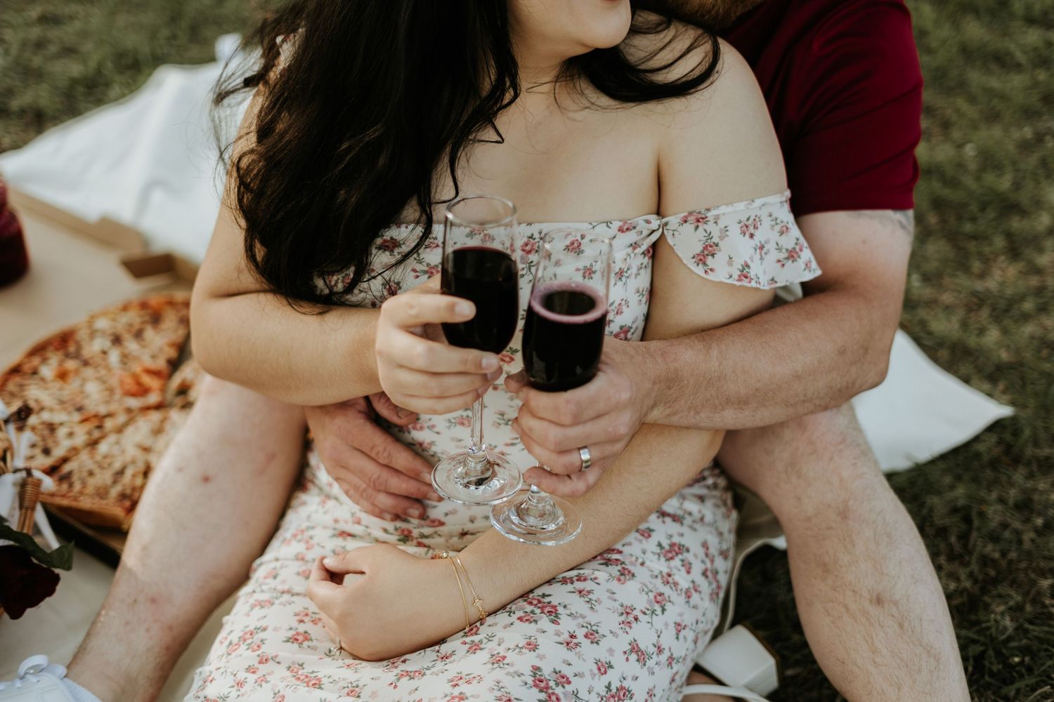 A couple shares an intimate moment on a picnic blanket in a grassy outdoor setting.