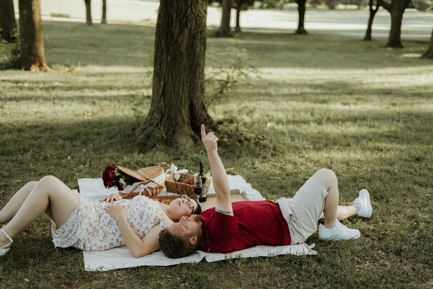Two people relax on blankets under shady trees in a peaceful park setting on a summer afternoon.