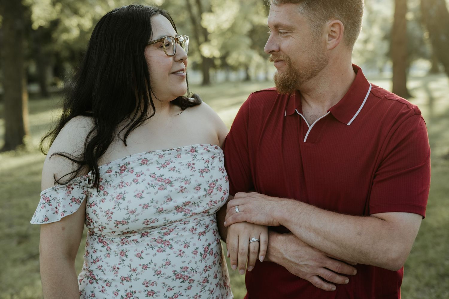 A couple shares tender moments in a park setting while wearing red and floral outfits during a romantic photoshoot.