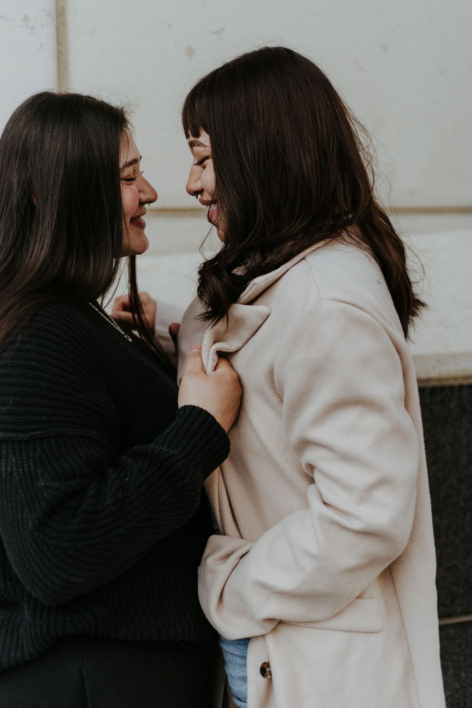 Two people in winter coats sharing an intimate moment against a light background.