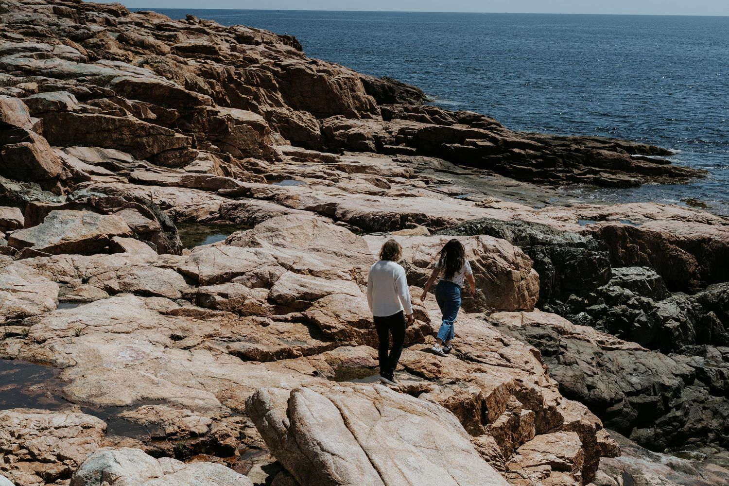 A person explores the rugged coastal rocks along the ocean shore on a sunny day.