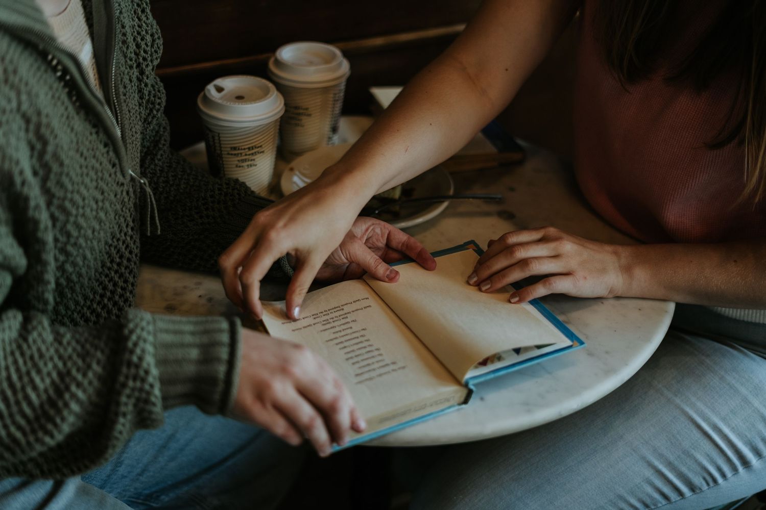 Someone writing in a notebook with a coffee cup nearby while sitting at a wooden table in warm lighting.
