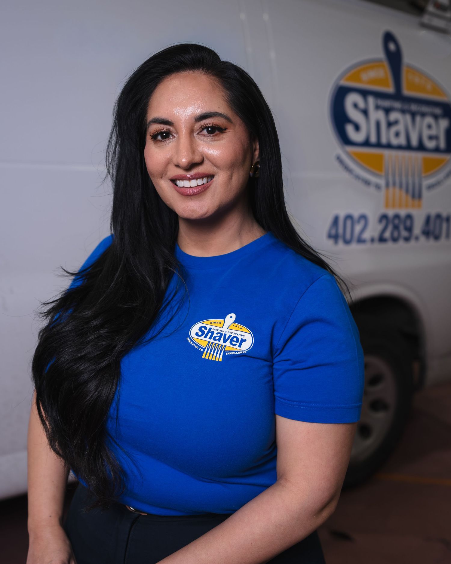 Woman in blue Shaver company t-shirt smiling in front of branded service van with phone number.