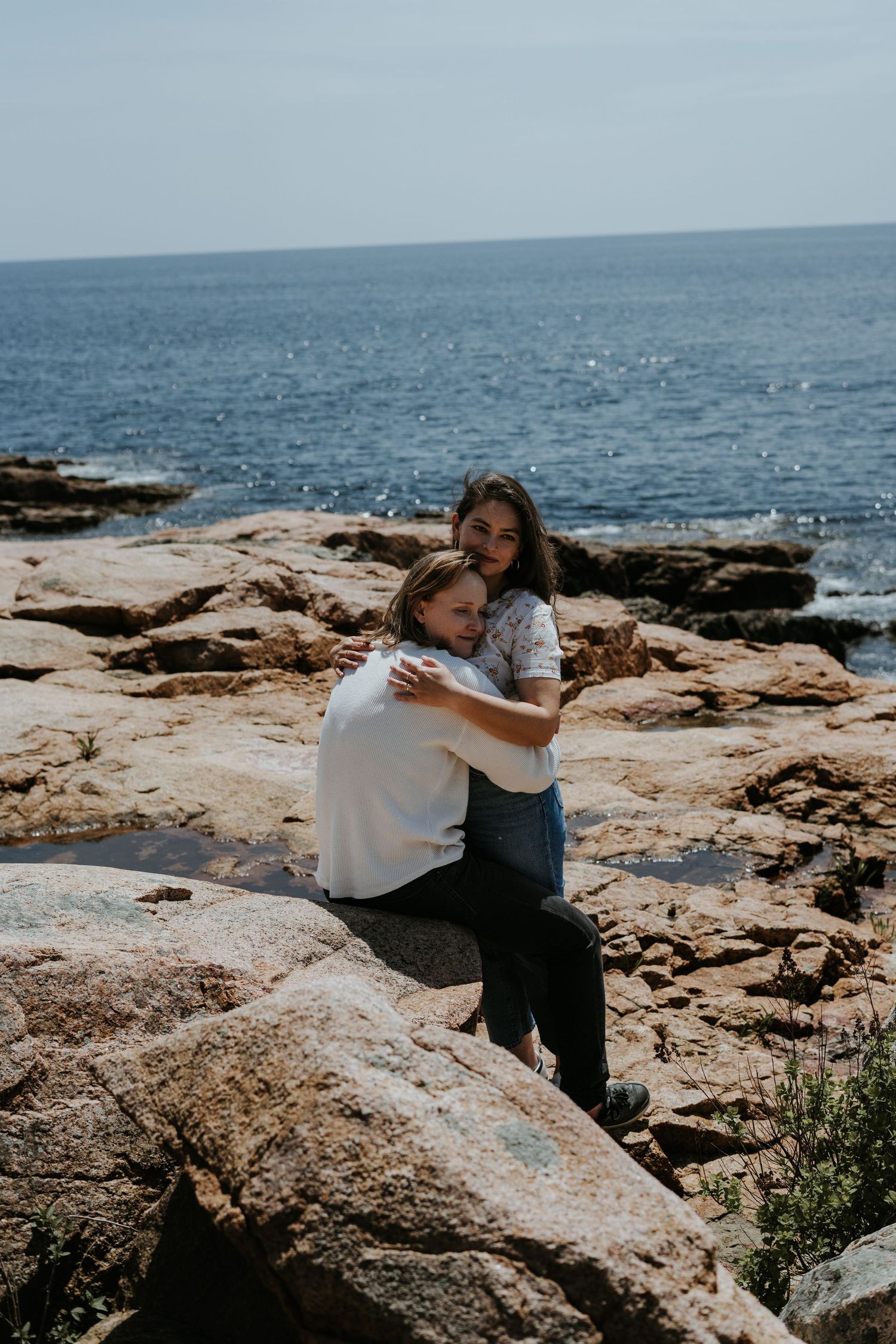 Person in white sweater and dark pants climbing on coastal rocks with ocean waves in the background.