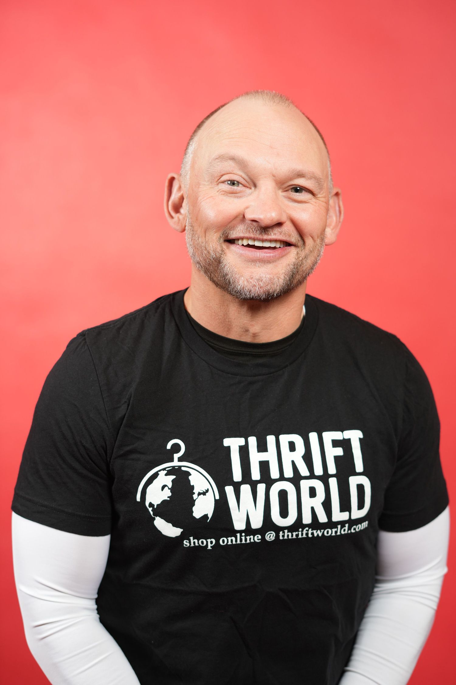 Smiling bald man wearing a black Thrift World t-shirt against a red background.