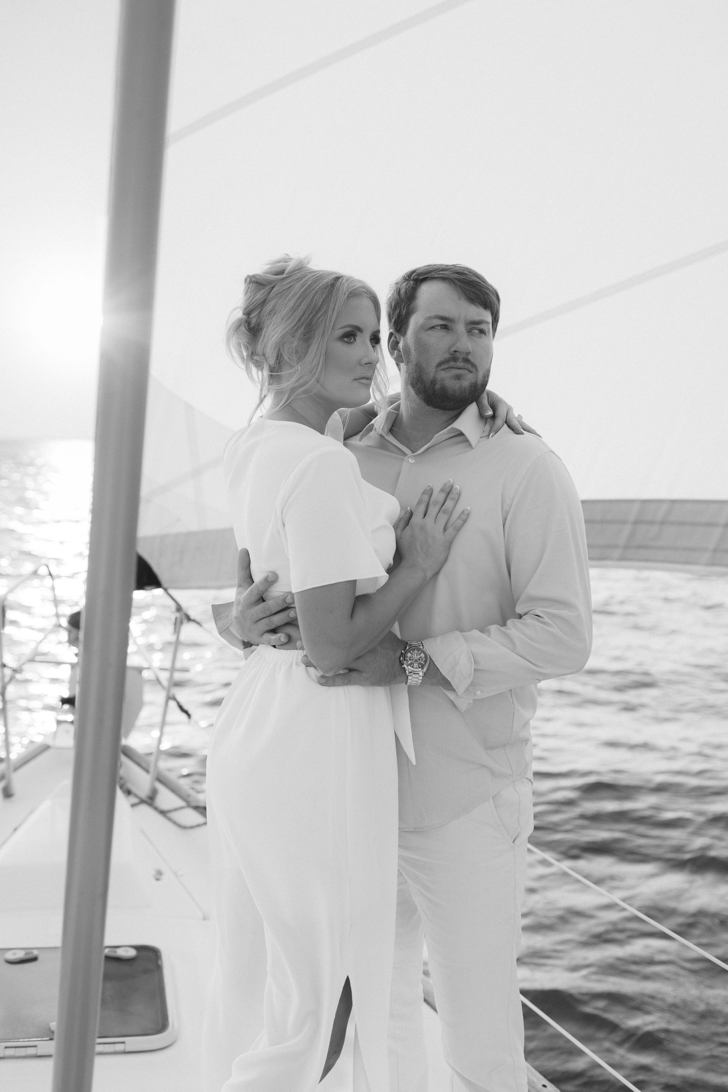 Black and white photo of couple embracing on sailboat deck at sunset on open water.