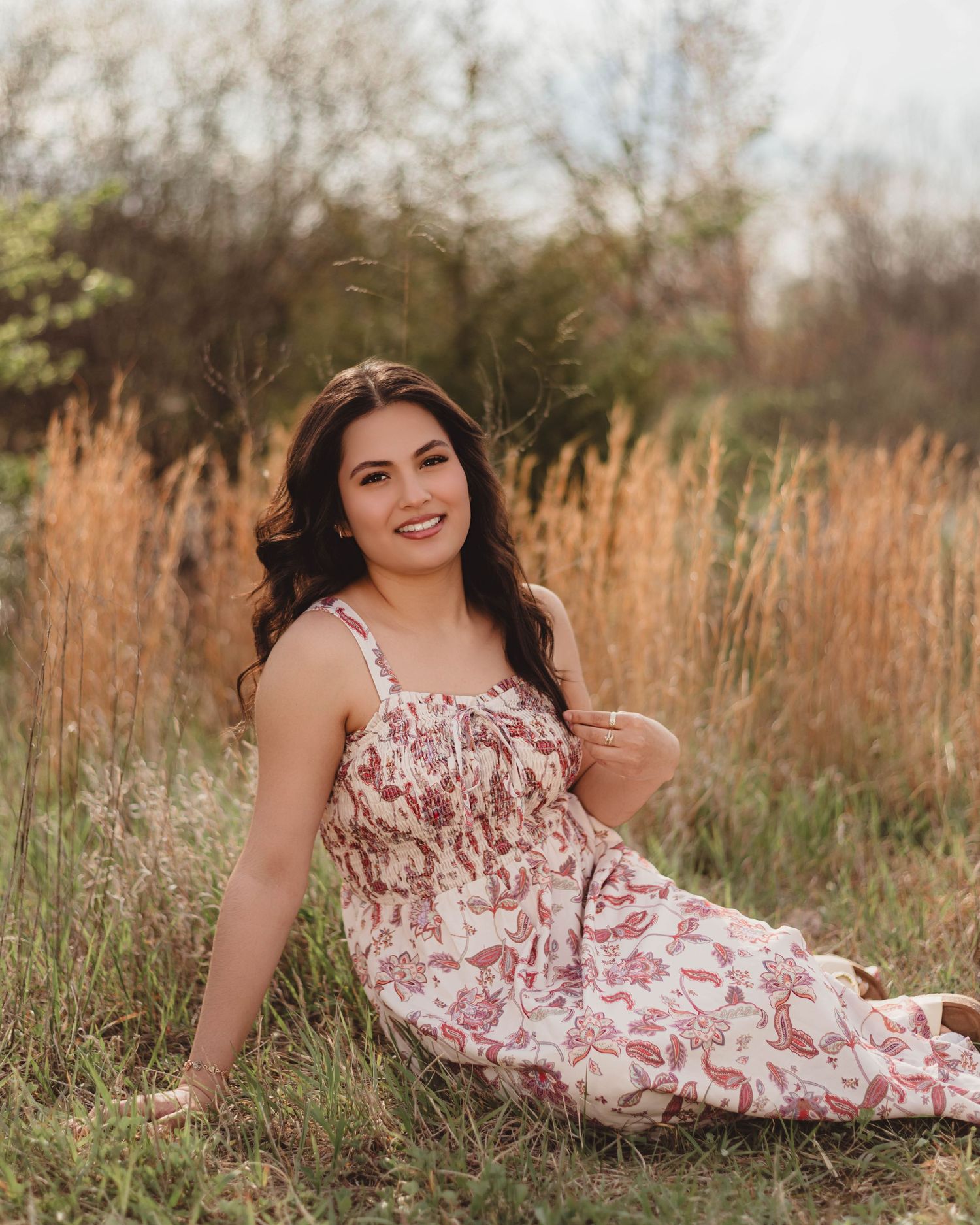 High School Senior in floral maxi dress sitting gracefully in a golden grass field for senior portrait photography in Lafayette, Indiana.