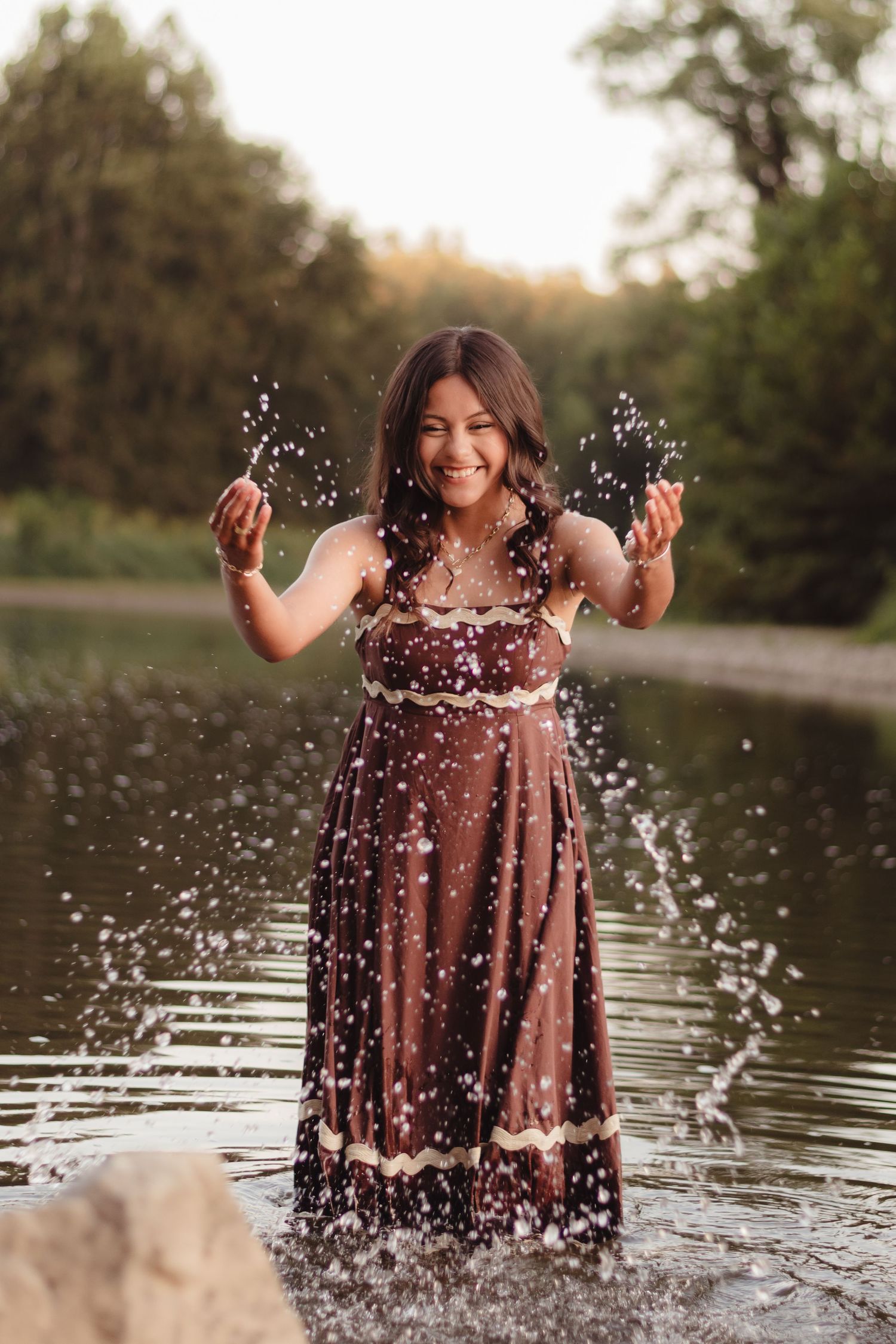 High school Senior joyful splashing creates water droplets during a sunset photoshoot by a lake in Lafayette, Indiana.