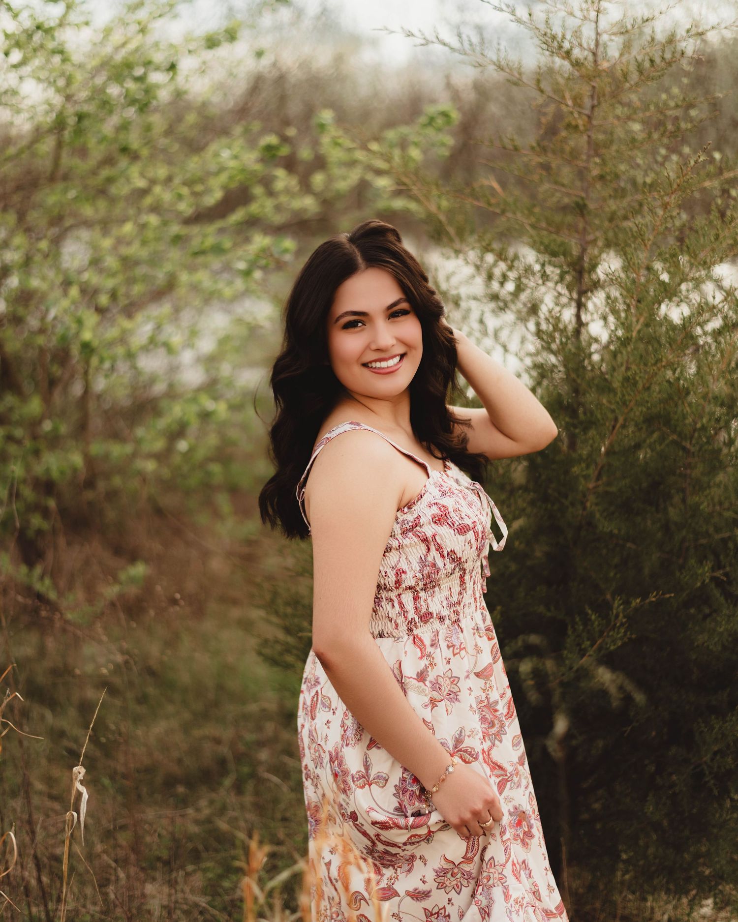 Young woman in floral sundress smiling outdoors among lush green trees in a natural setting in Lafayette, indiana