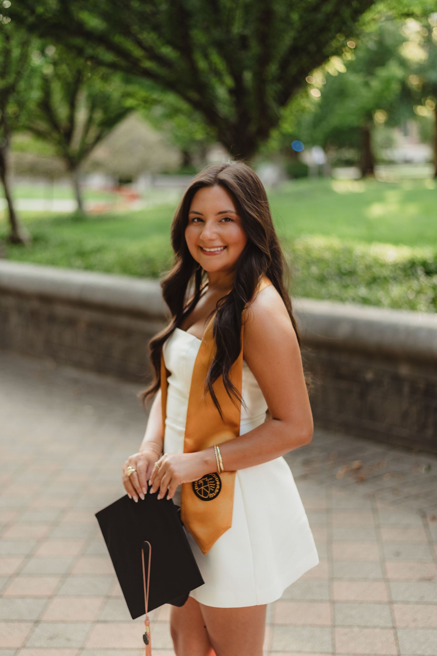 A person in a mustard yellow top and white skirt sits on stone steps in an outdoor garden setting at Purdue Campus in West Lafayette, IN.