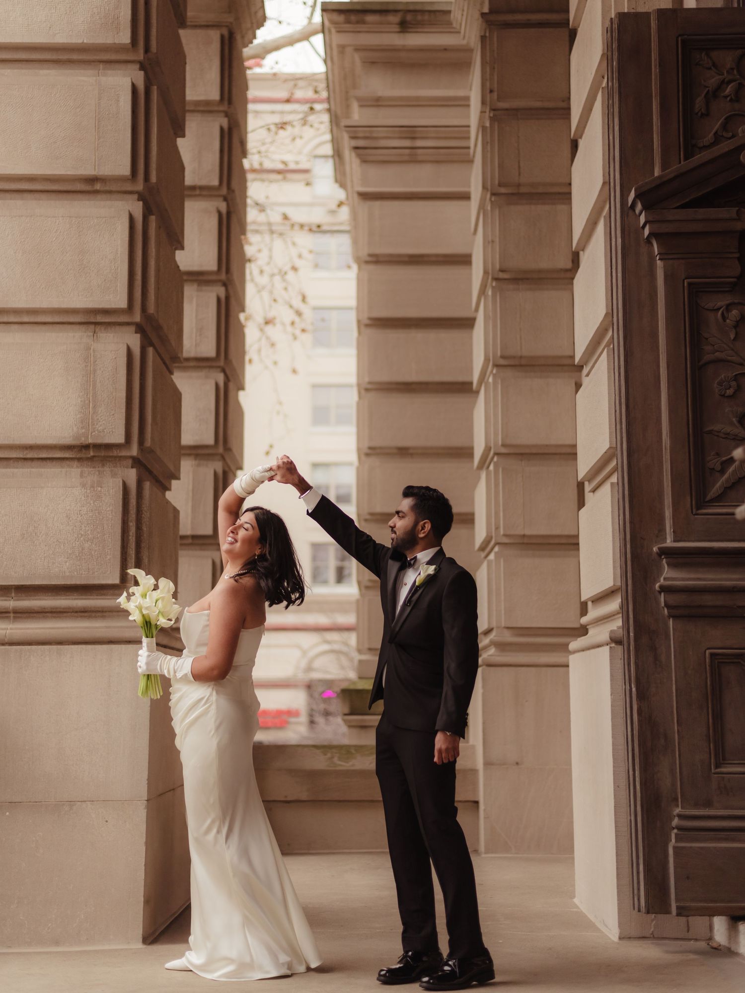 Bride and groom between grand stone columns, bride in white gown holding bouquet, groom in black tuxedo at the Tippecanoe Courthouse.