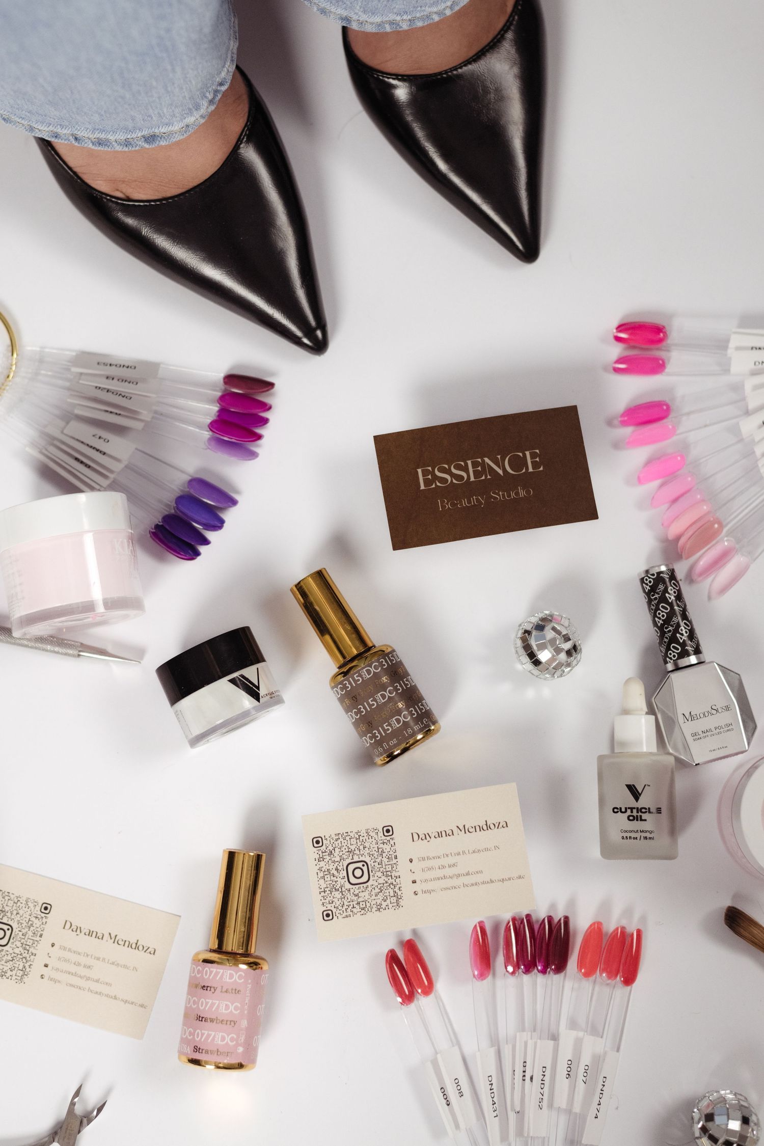 Flat lay of nail polish, gel products, color swatches, and Essence Beauty Studio business cards with black heels.