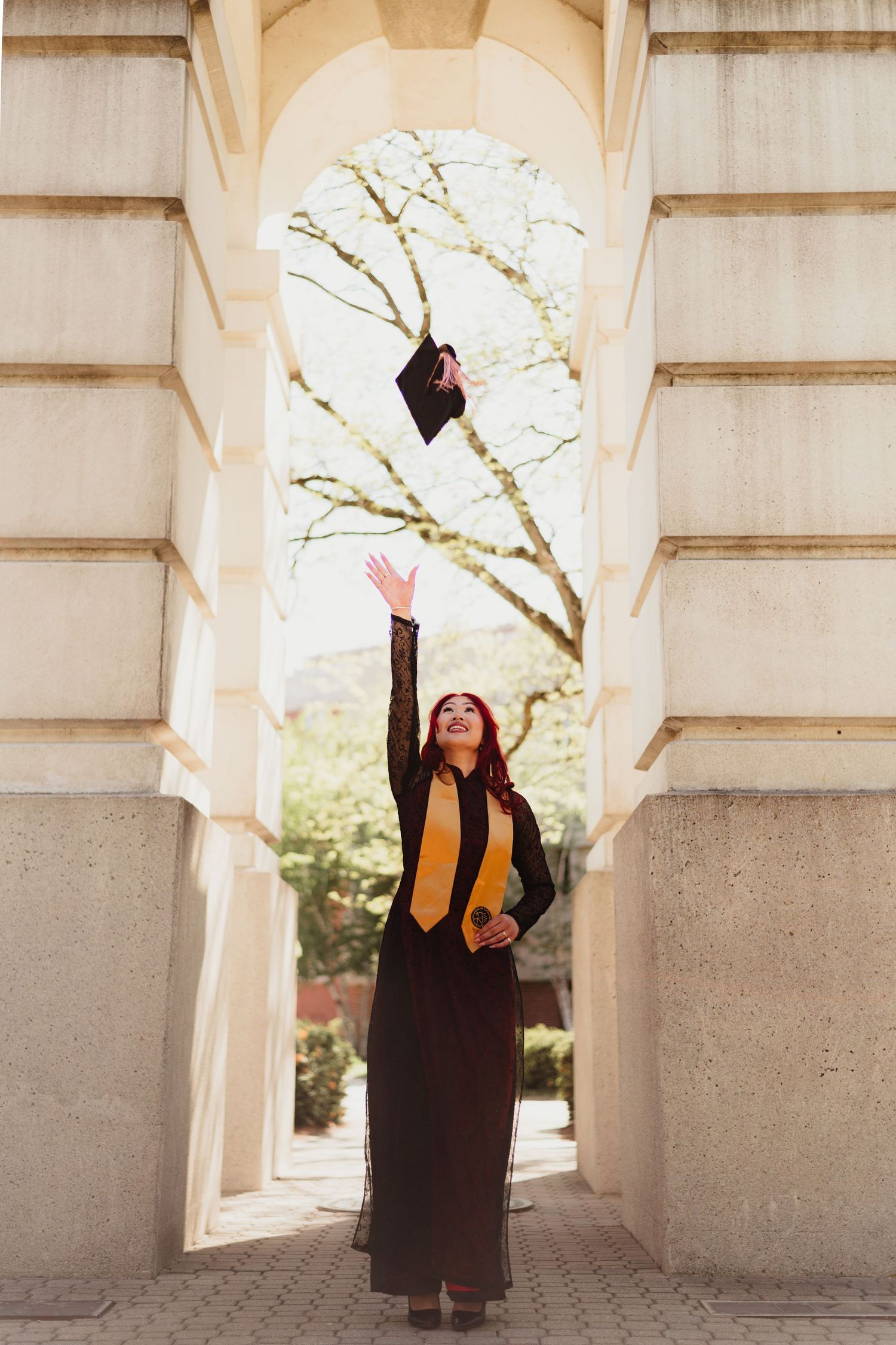 Graduate in cap and gown celebrates under stone archways during commencement ceremony at Purdue University.