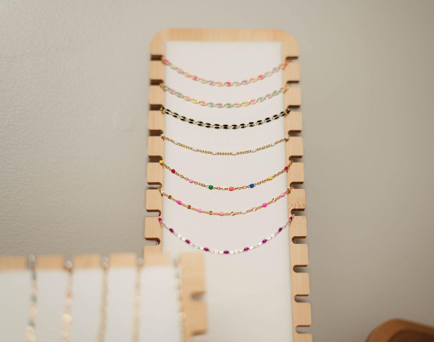 Colorful beaded necklaces displayed on a wooden jewelry holder with notched slots against a neutral wall.