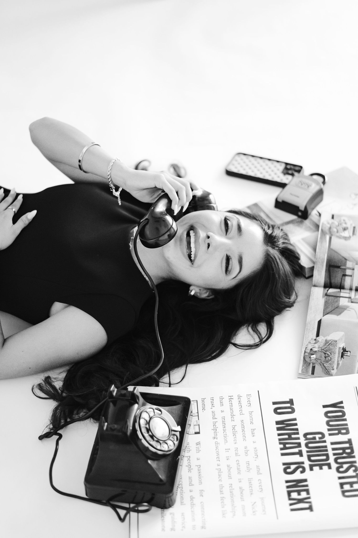 Black and white photo of a laughing woman lying down, holding a vintage rotary phone to her ear.