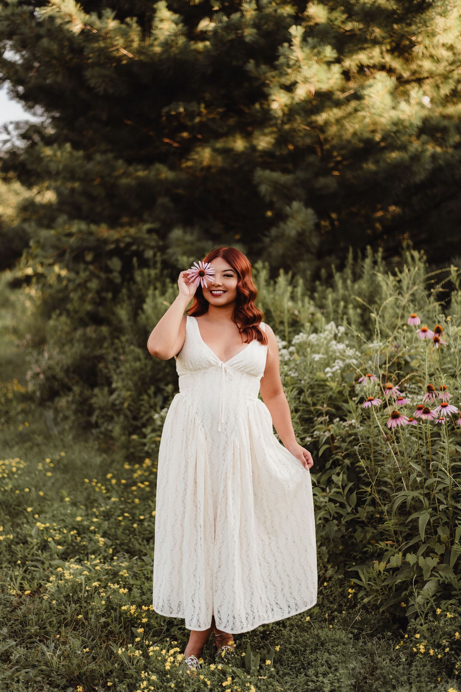 Woman in white lace dress holding a flower in a wildflower garden at golden hour.