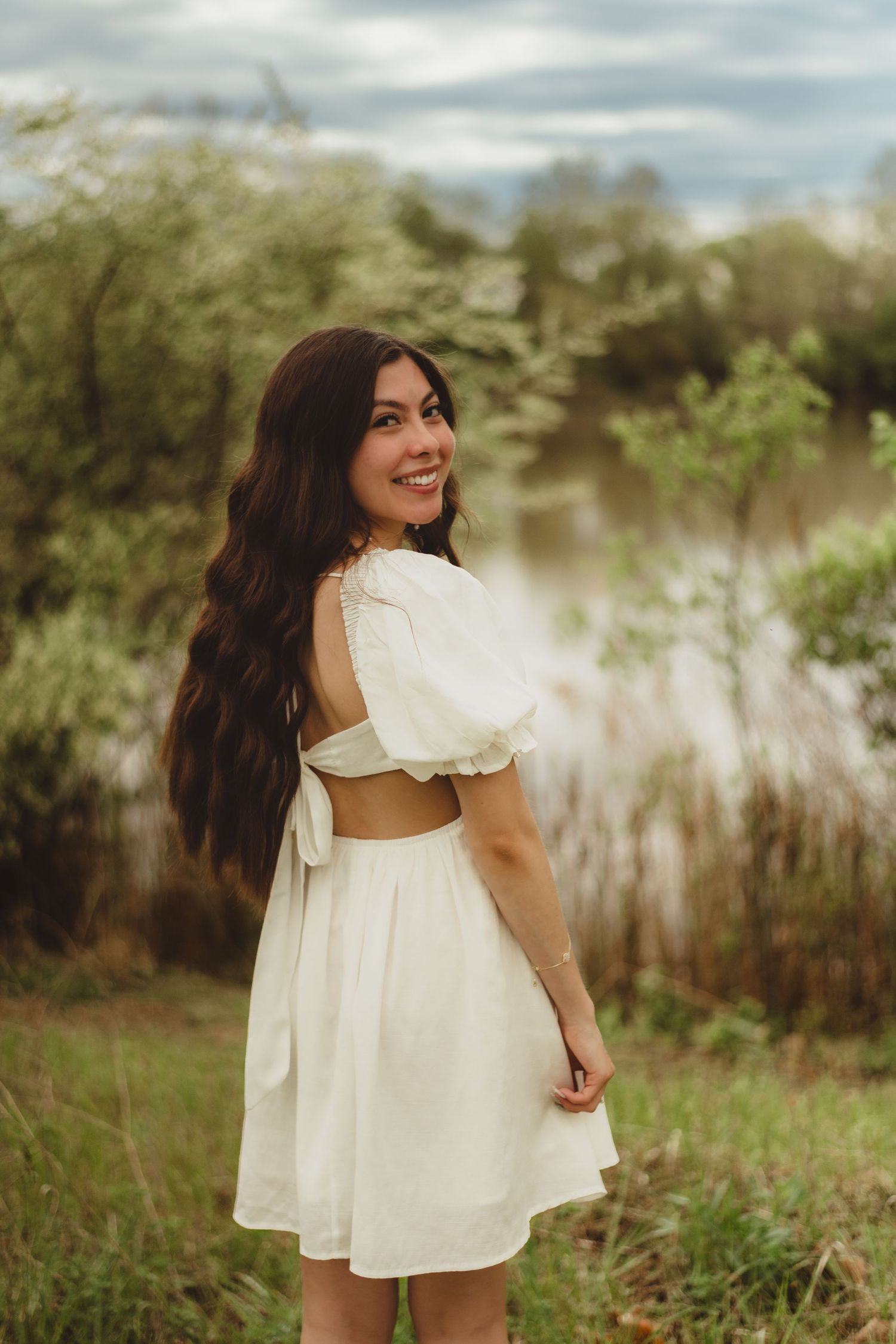 A white summer dress with cutout back detail photographed in a dreamy outdoor setting with tall grass and soft lighting.