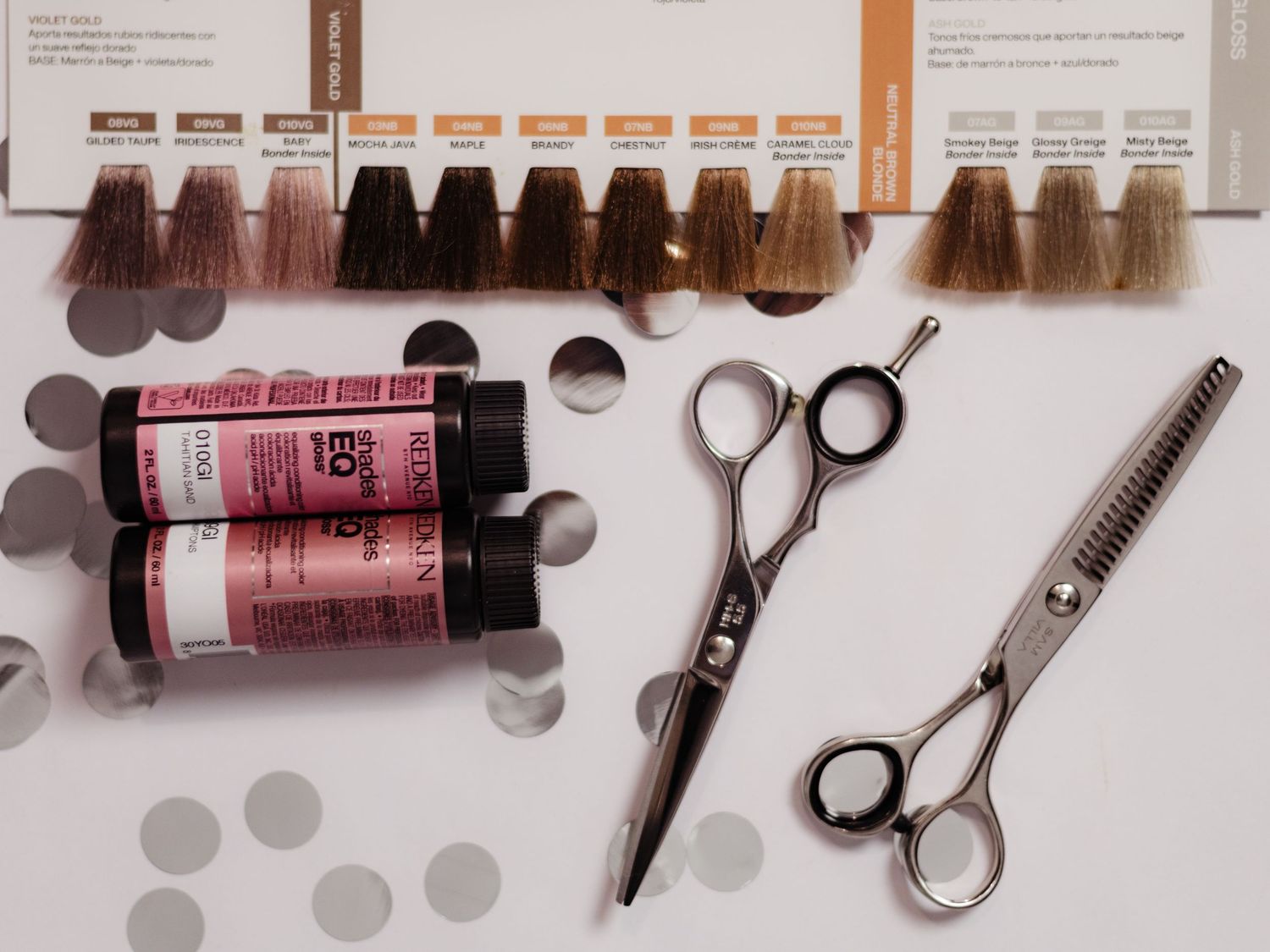 Hair dye bottles, color swatches, and professional scissors arranged on a white surface for salon hair coloring.