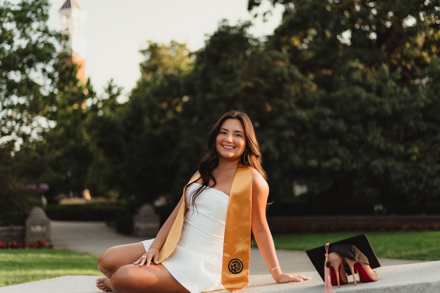 Purdue Graduate  in a white dress sits on engineering fountain at Purdue Campus in West Lafayette, Indiana.