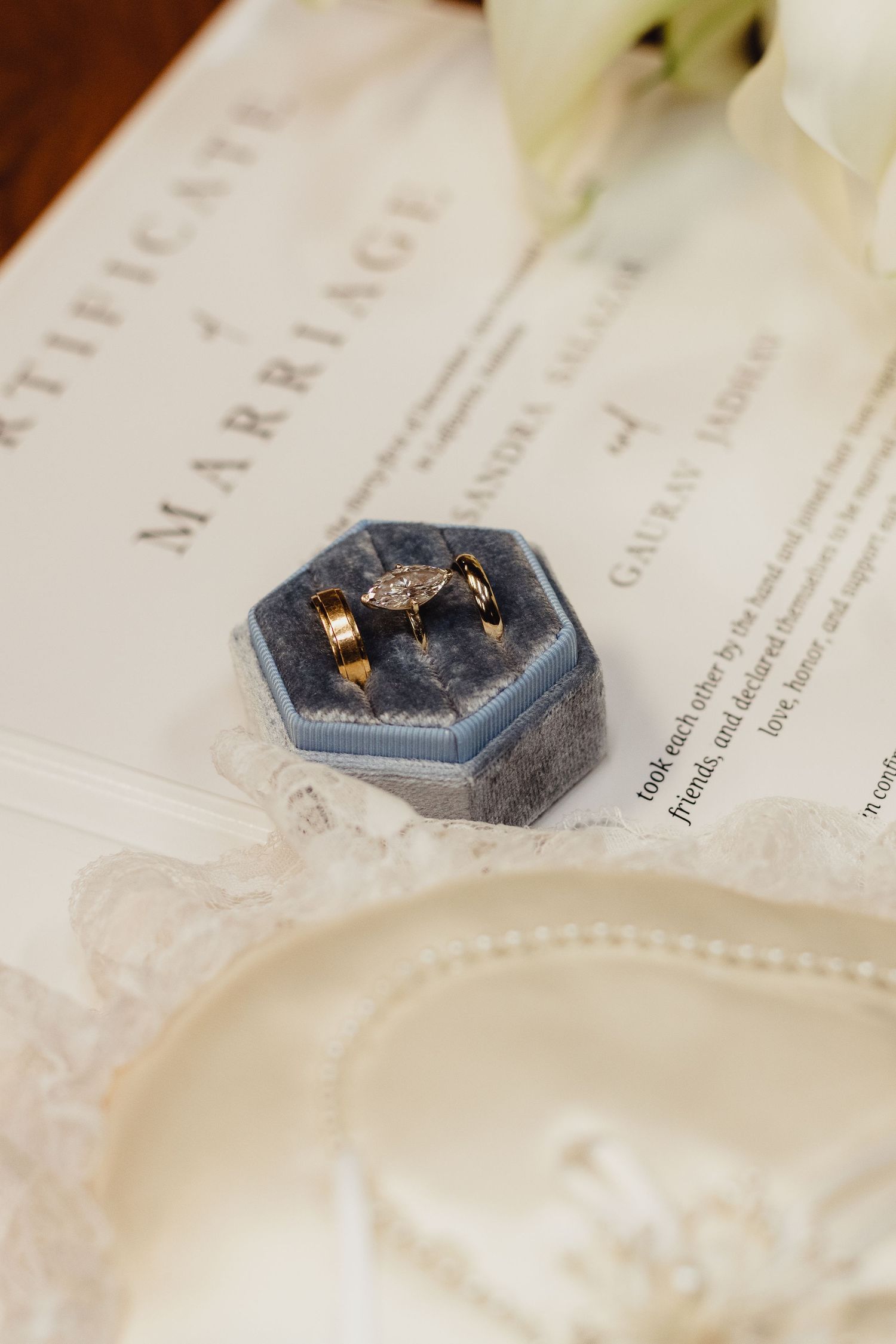 Close-up view of delicate wedding rings nestled in a hexagonal blue velvet ring box on white paper.