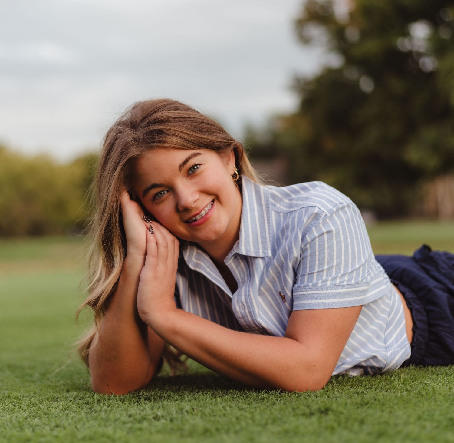 Person in striped shirt lying on grass in outdoor setting with warm natural lighting.