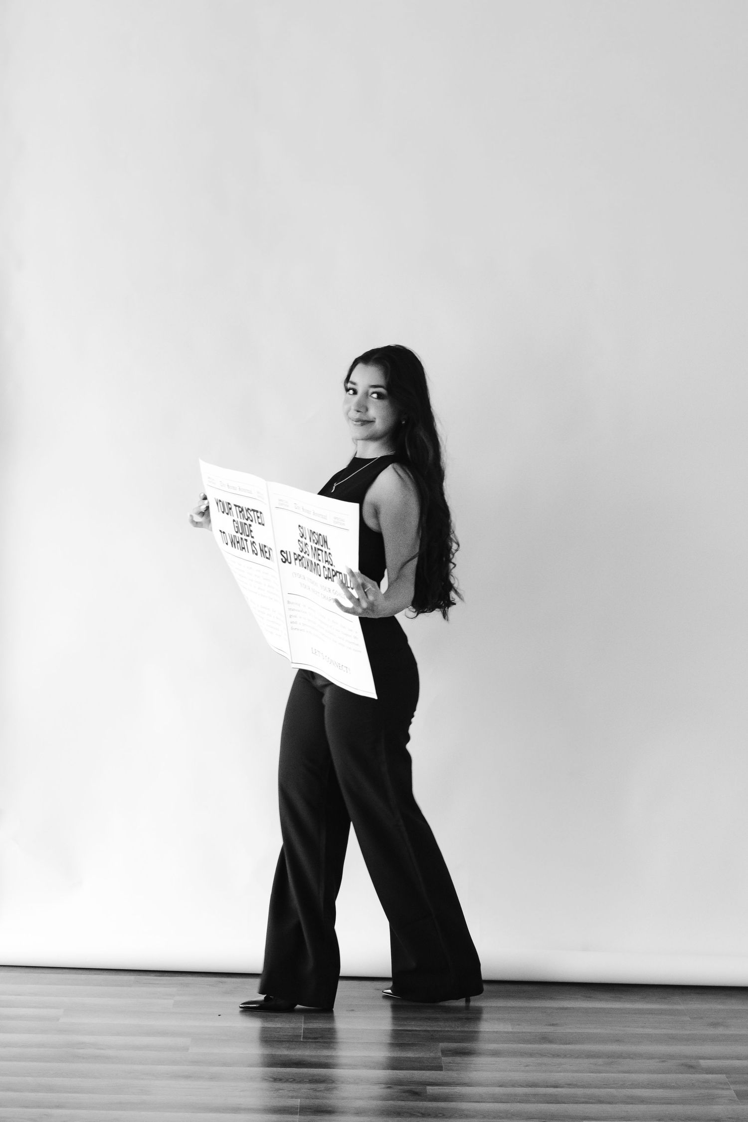 Woman in black outfit holding a large sign, standing against white wall in black and white photo.