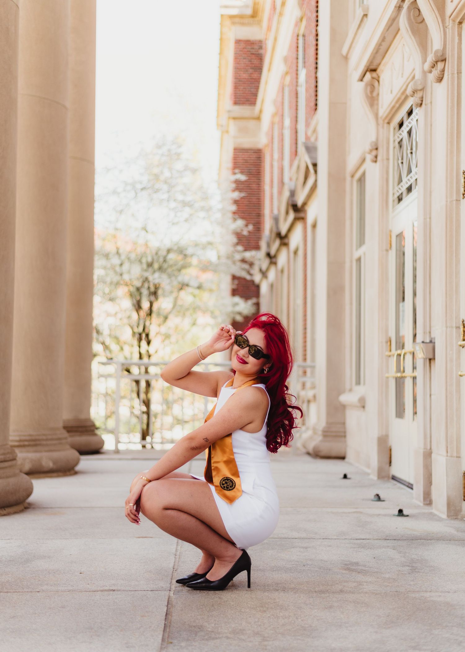 A figure in a white dress and red hair poses playfully in a series of shots along a columned building hallway  at Purdue Campus.