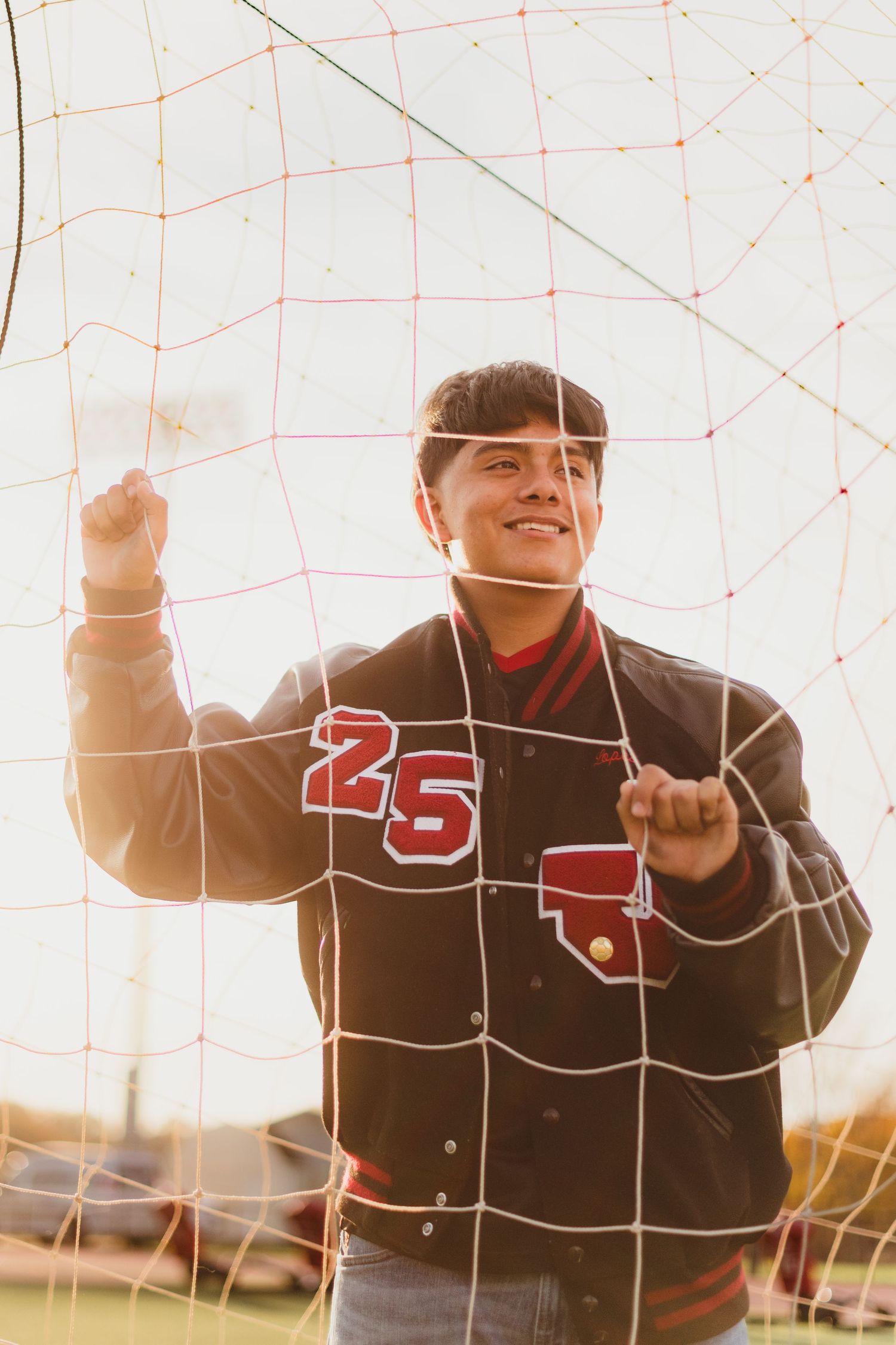 Baseball players in uniforms celebrate together at sunset through a wire fence.