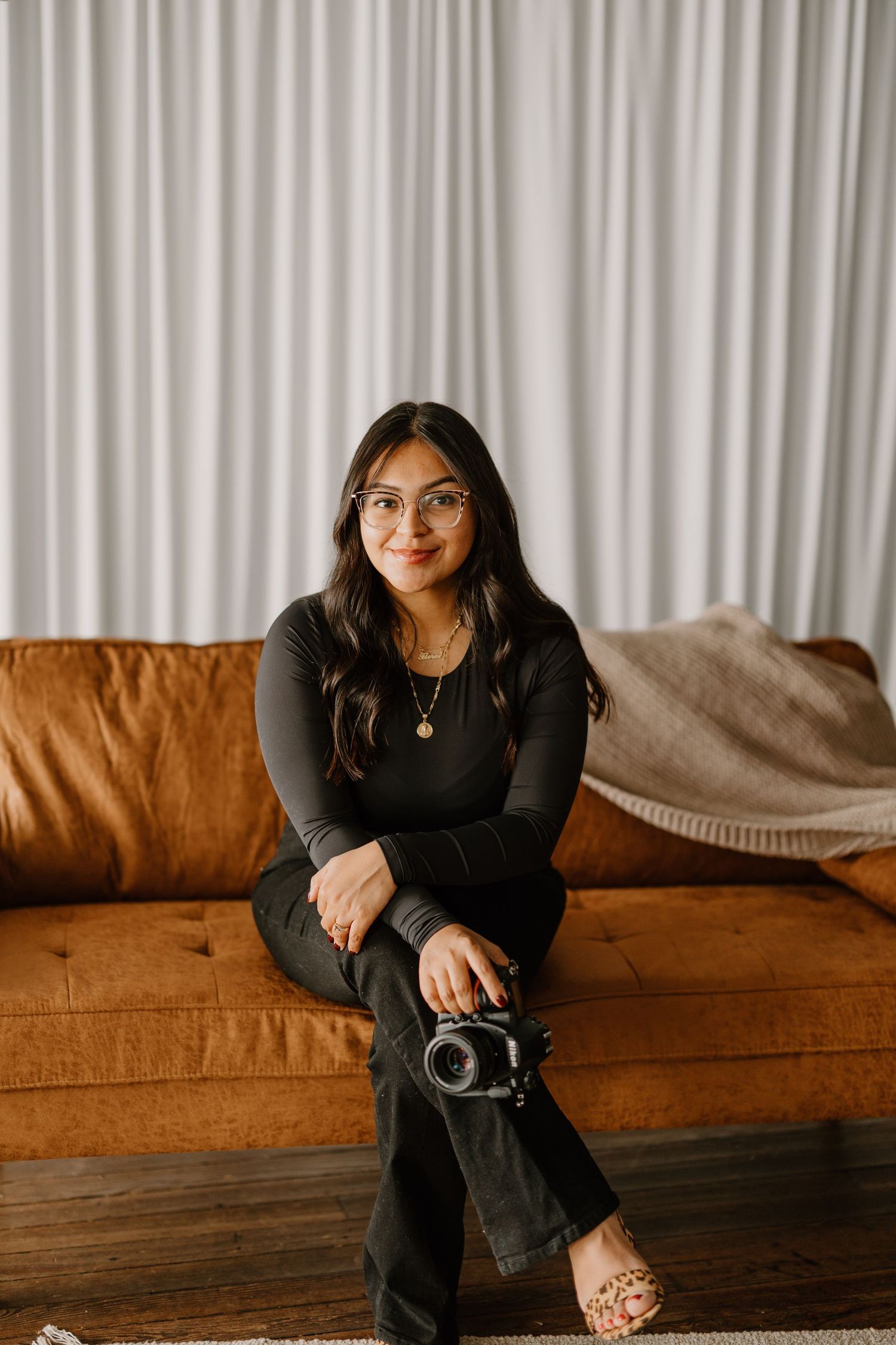 Person in black attire sits on brown leather couch in modern living room setting.